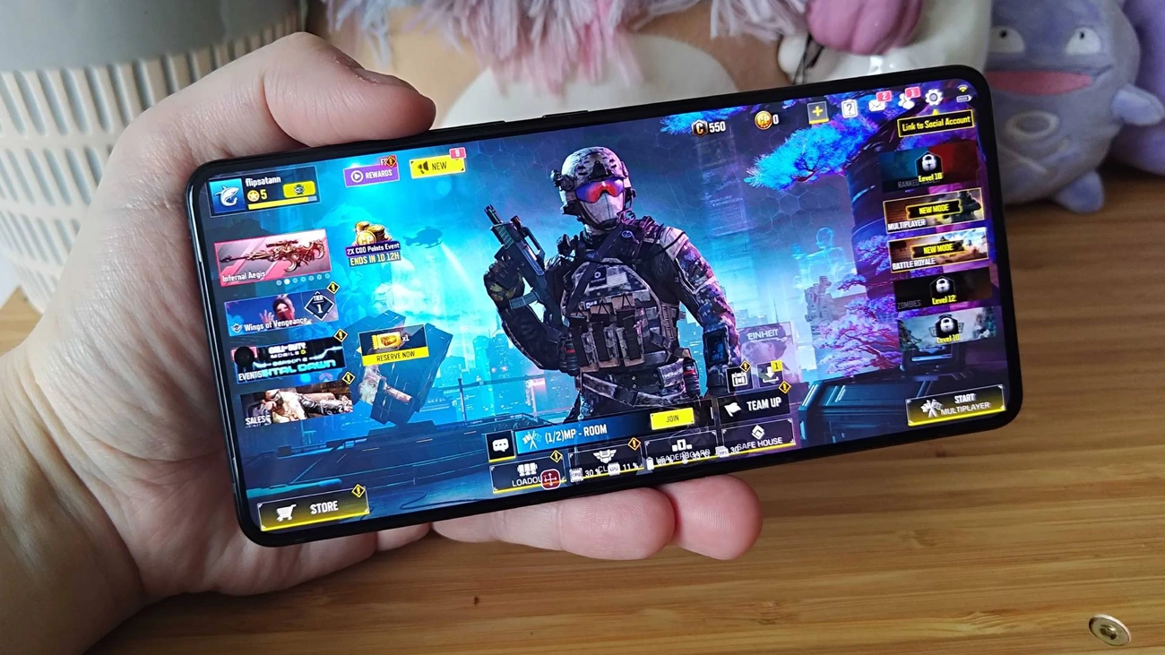Hand holding a smartphone displaying a futuristic soldier in a first-person shooter game menu screen.