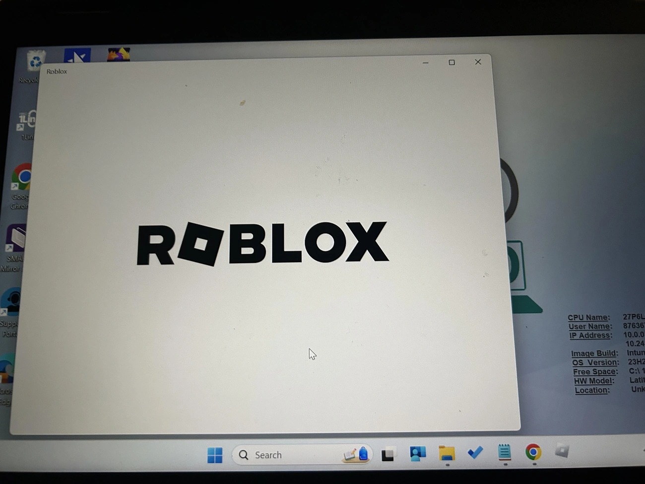 Pantalla de carga de Roblox mostrada en una computadora portátil de la escuela con íconos de escritorio e información del sistema en segundo plano.