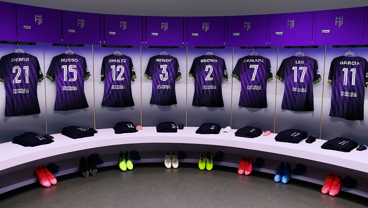 Les maillots rayés violets et noirs de Football Manager sont accrochés dans un vestiaire, chacun avec les noms et les numéros des joueurs.
