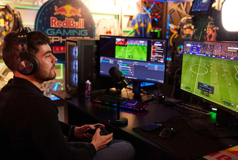 Un joueur jouant à EA FC 26 sur deux écrans avec la marque Red Bull Gaming dans une configuration de jeu professionnelle.