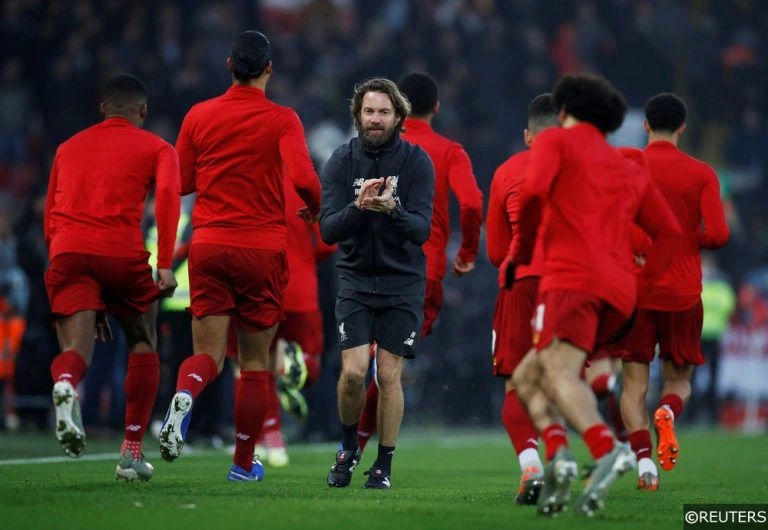 Entraîneur de football en noir menant un groupe de joueurs de football en rouge lors d'un entraînement sur un terrain en herbe.